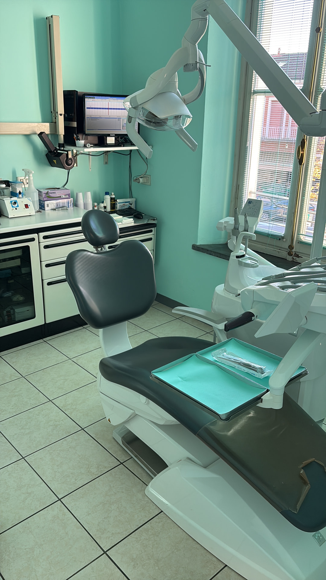 Sala operativa reale dello studio dentistico con poltrona odontoiatrica, lampada, attrezzatura e pareti verde acqua